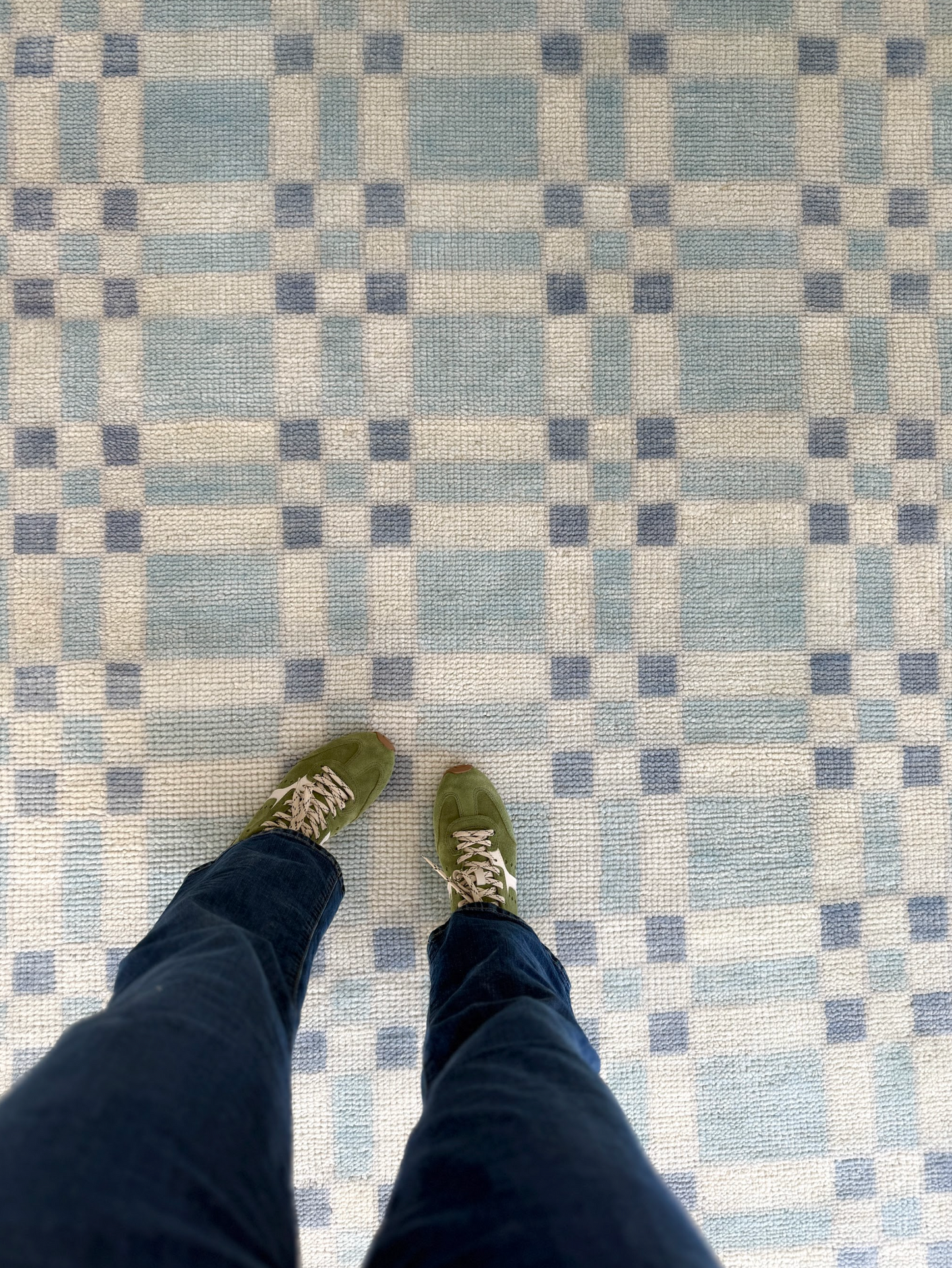 Checkered patterned rug with a person wearing green shoes and dark pants standing on it.