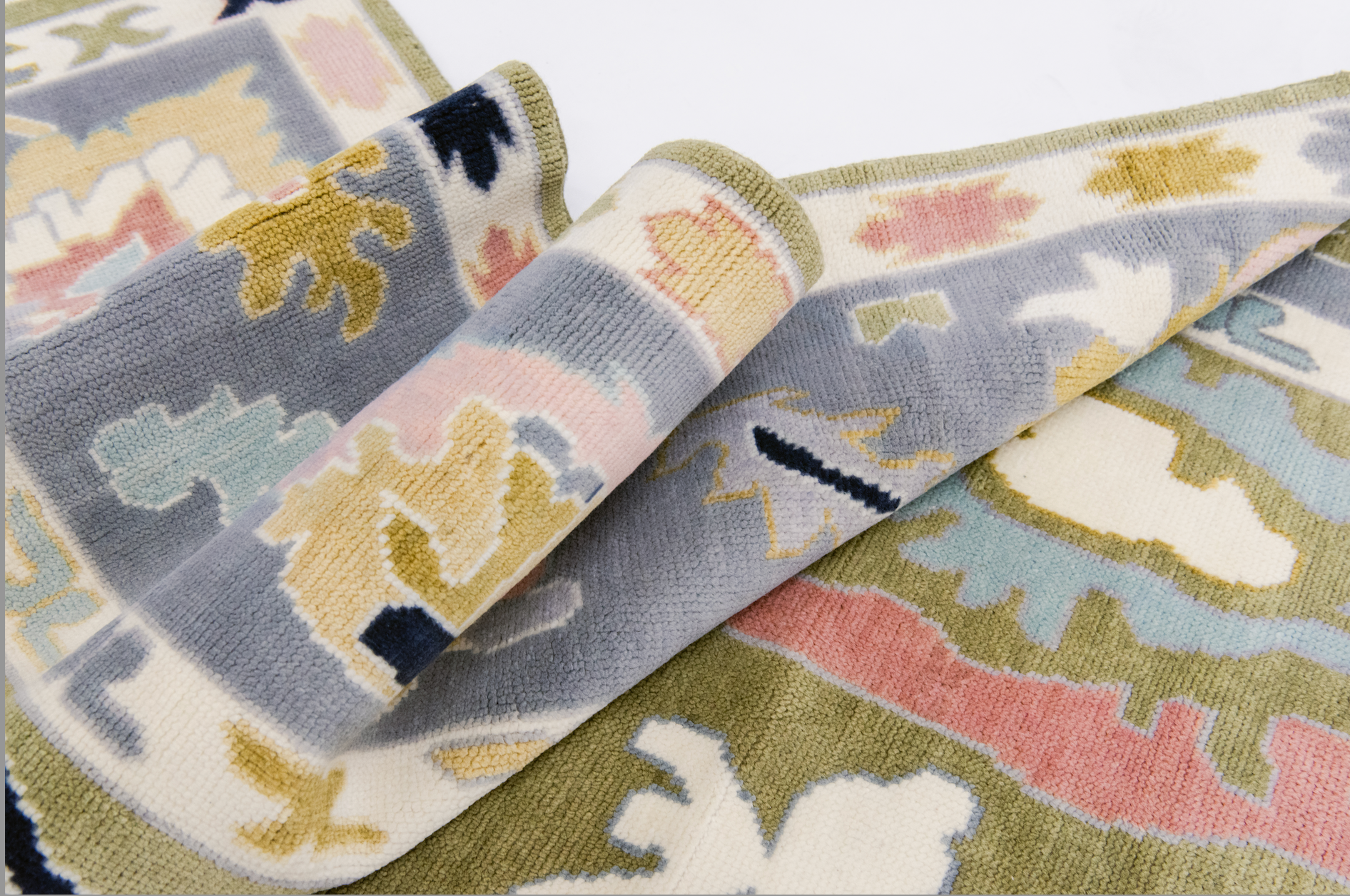 A close-up view of a Penny Modern Oushak rug showcasing its hand-knotted wool texture and the oversized Oushak motifs in various colors including blush, navy, and pale lilac on an olive green background.