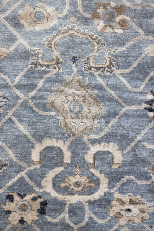 A close-up image of a hand-knotted rug with a floral pattern in a mix of blue and neutral tones.