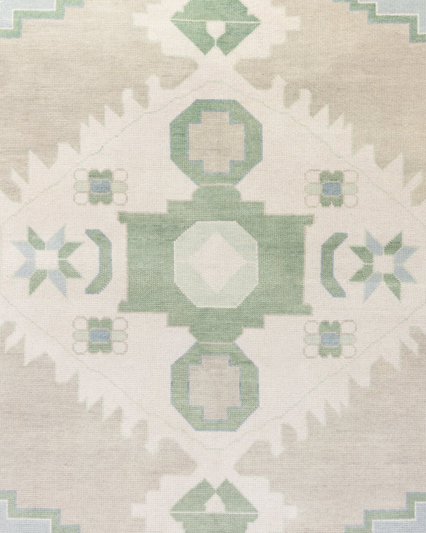 Close-up view of a handcrafted area rug with a geometric medallion pattern and crescent motifs in sage green, soft taupe, and creamy ivory colors.